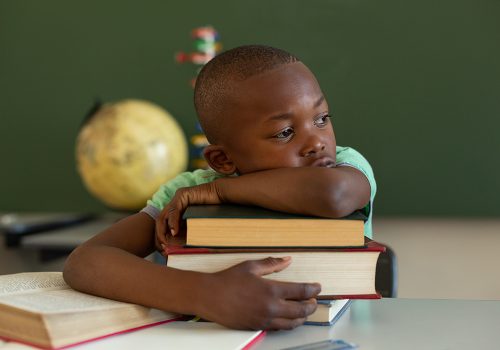 Front view of African American  schoolboy leaning on books at desk in a classroom at elementary school