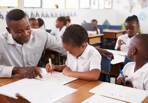 teacher-helping-elementary-school-girl-at-her-desk